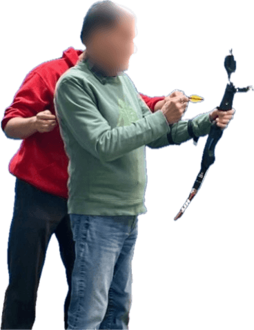 Lukas Chang stands behind a para athlete and guides the archer’s draw arm as they hold a recurve bow. The athlete’s face is blurred.