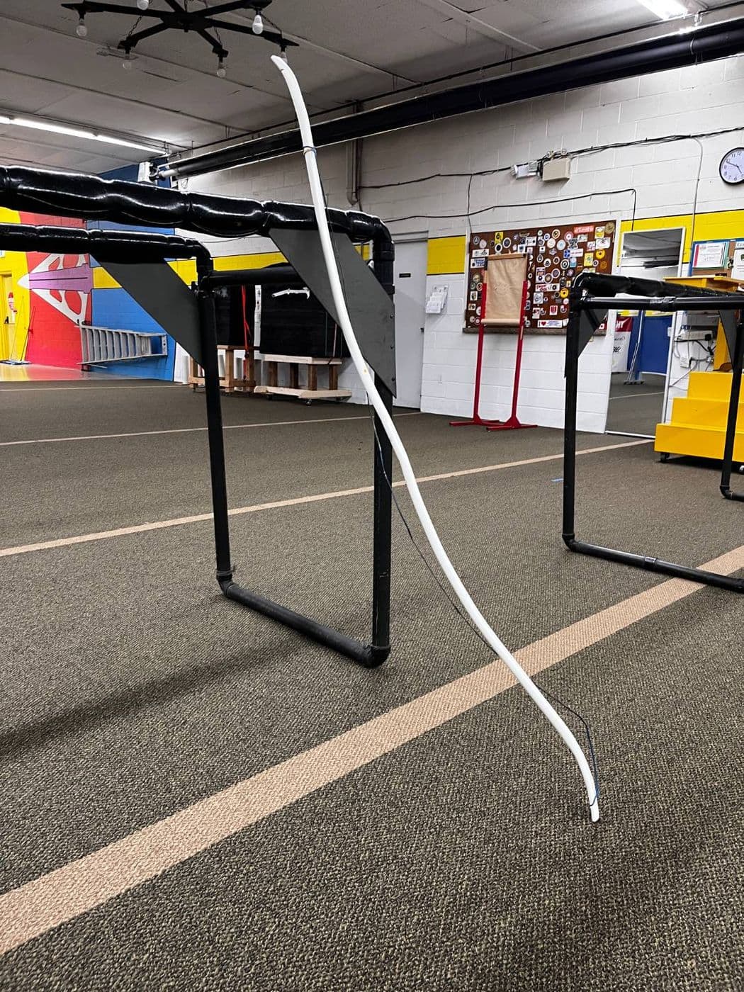 The finished LevelBow P1, a white PVC recurve with a dark string, leaning against a target stand on the indoor range.
